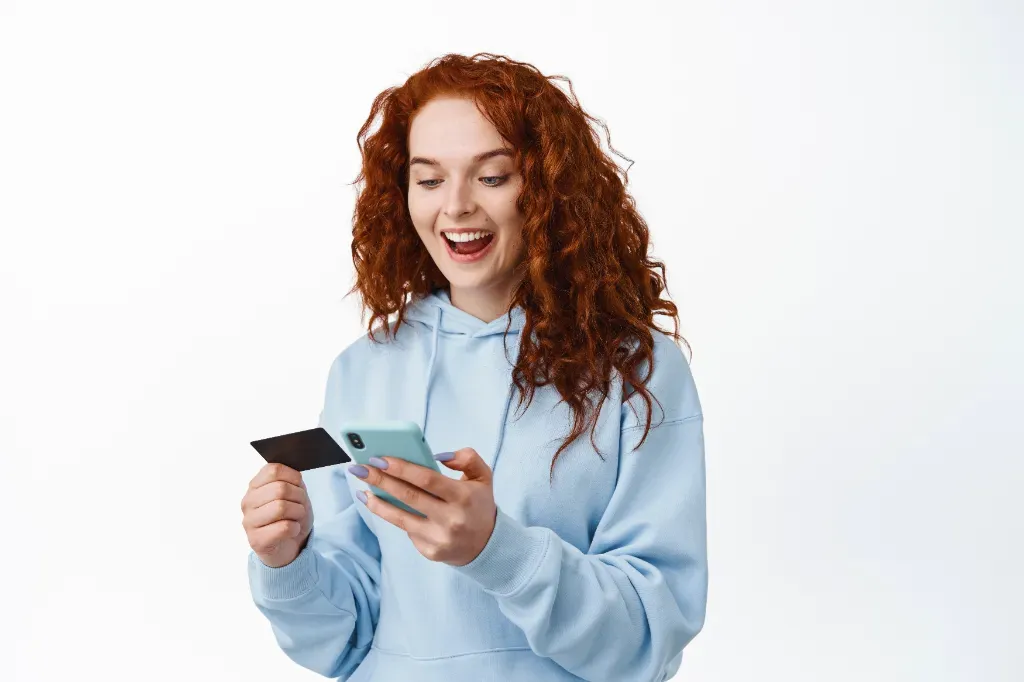 uśmiechnięta kobieta trzymająca w ręku telefon i kartę płatniczą